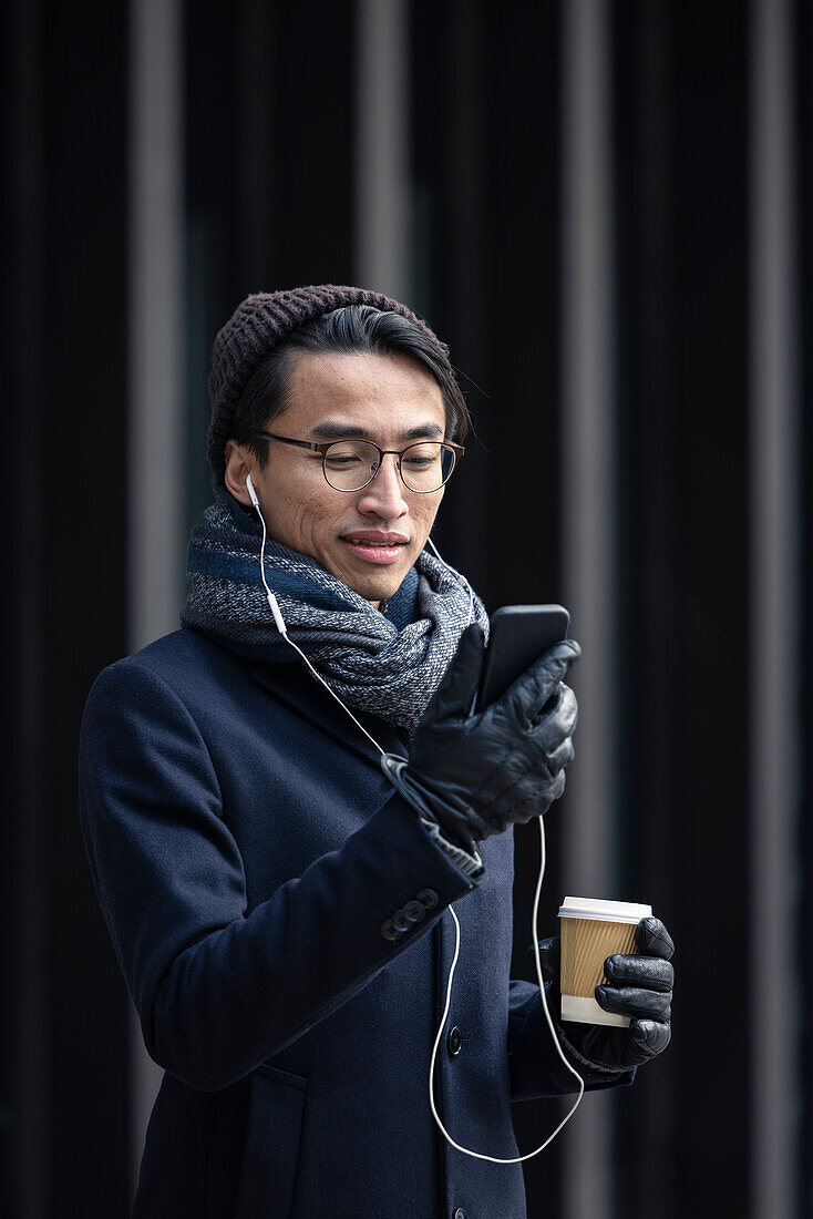 Handsome man with smartphone and paper cup on street