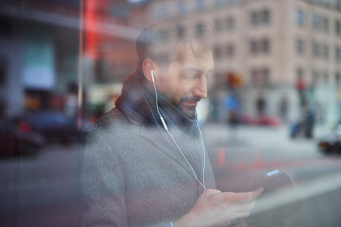 Eleganter Mann mit Smartphone, das sich im Fenster spiegelt