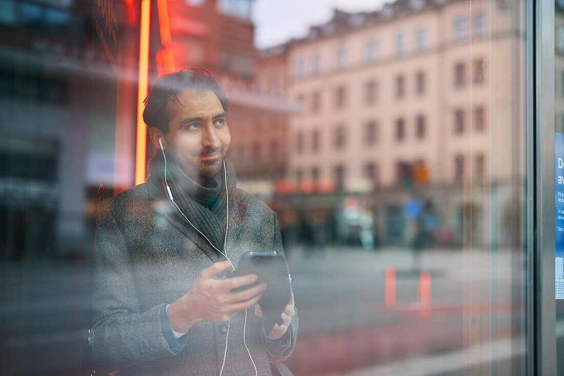 Eleganter Mann mit Smartphone, das sich im Fenster spiegelt