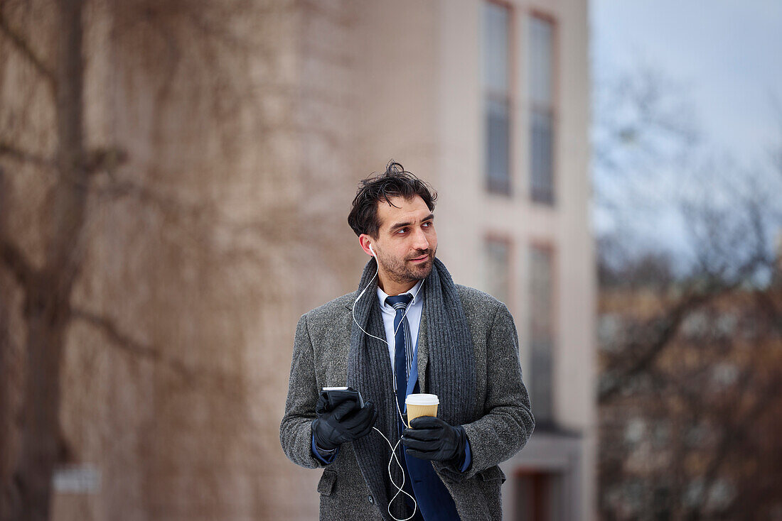 Eleganter Mann mit Smartphone und Pappbecher auf der Straße