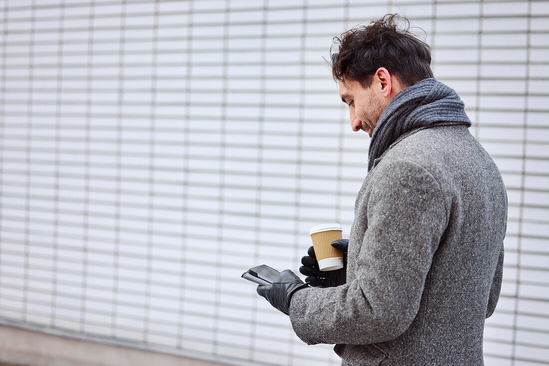 Eleganter Mann mit Smartphone und Pappbecher auf der Straße
