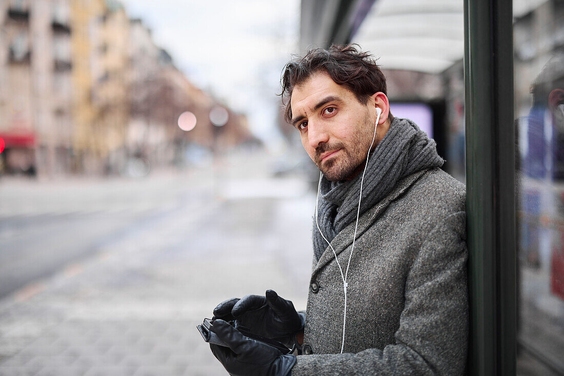 Elegant man with smartphone waiting on bus stop