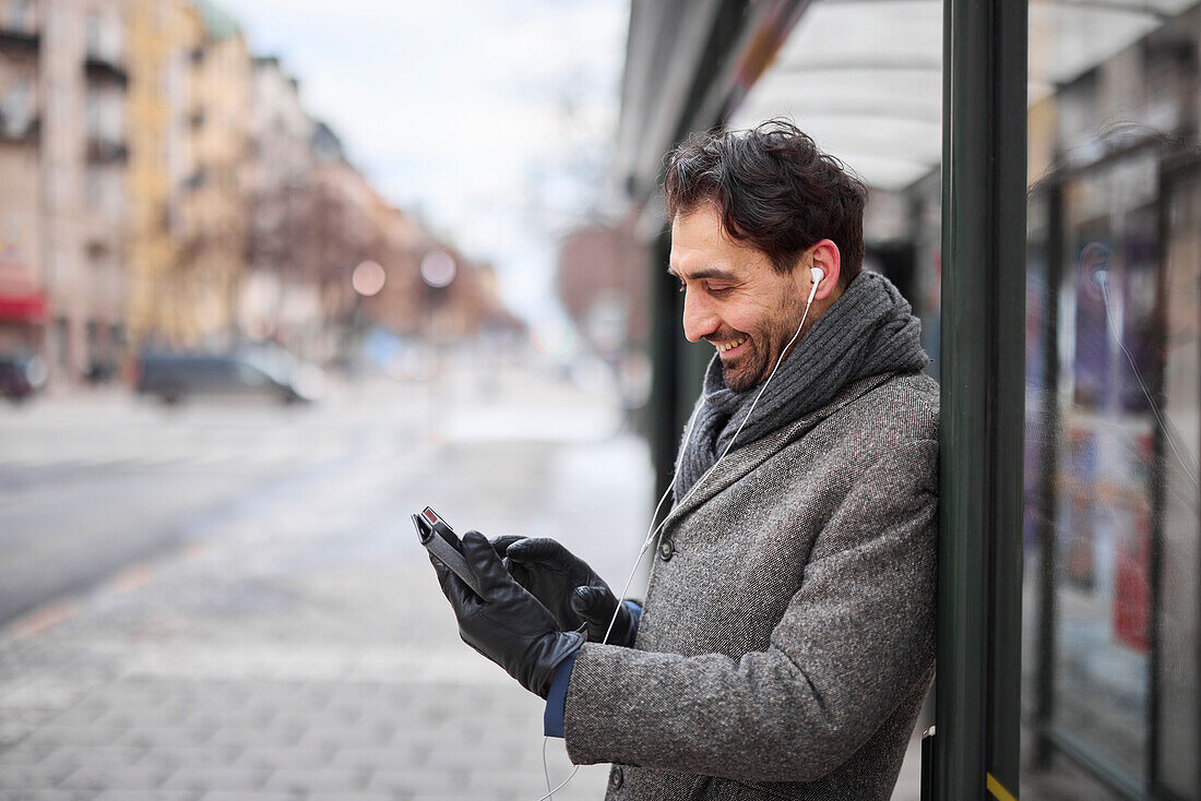 Eleganter Mann mit Smartphone an der Bushaltestelle