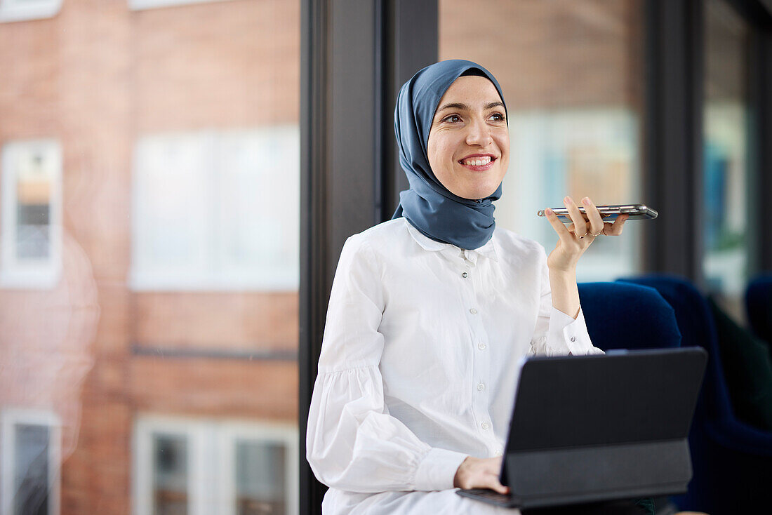 Geschäftsfrau im Hijab mit Telefon und digitalem Tablet im Büro