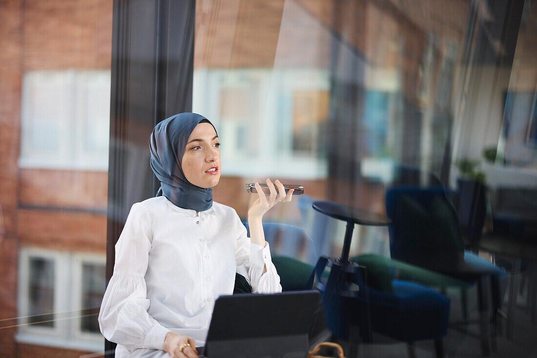 Businesswoman in hijab using phone and digital tablet in office