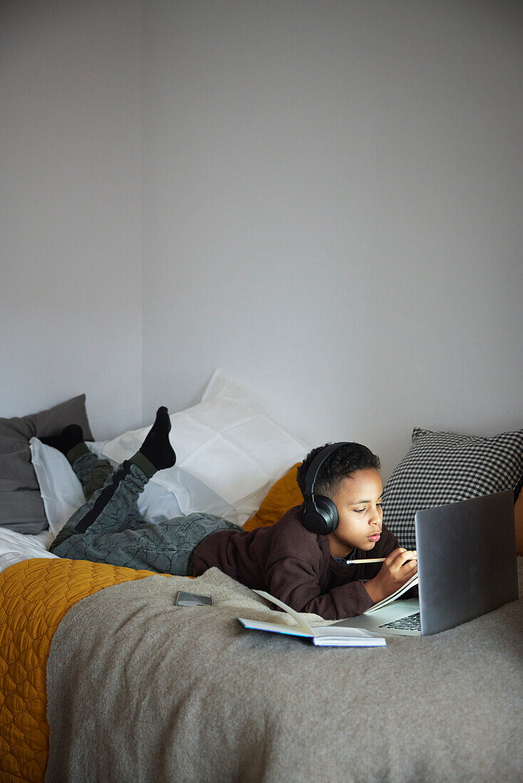 Boy doing homework with laptop in his bedroom