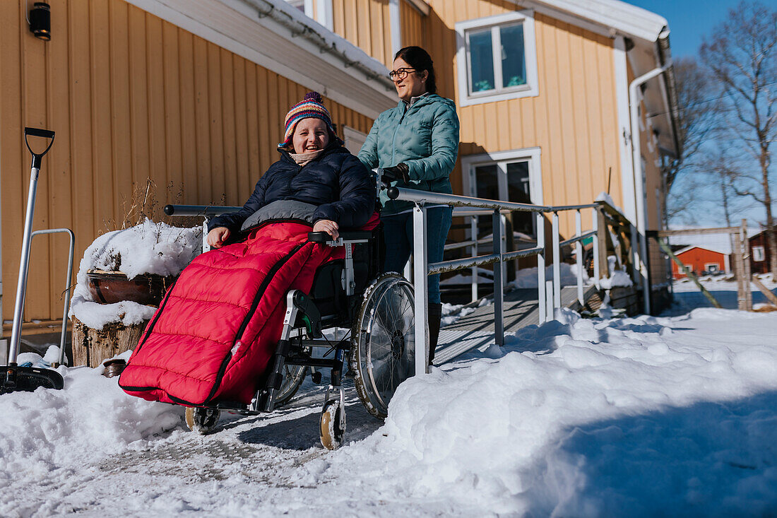 Mutter beim Winterspaziergang mit Tochter im Rollstuhl