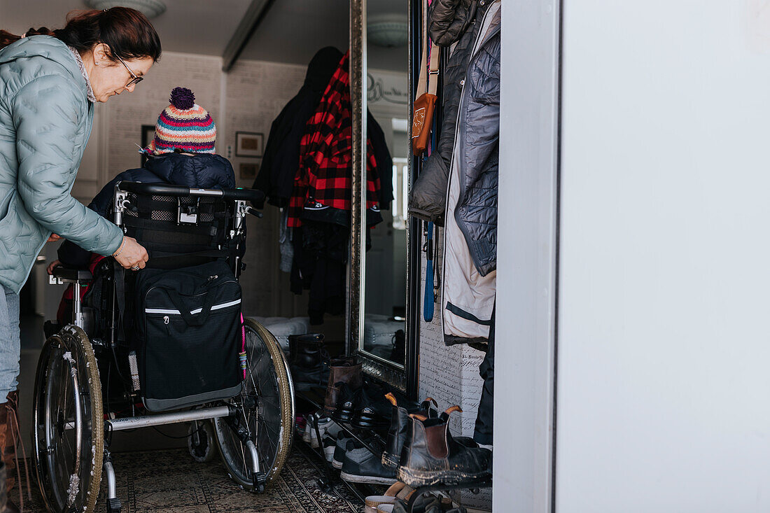 Mutter hilft Tochter im Rollstuhl beim Anziehen des Mantels