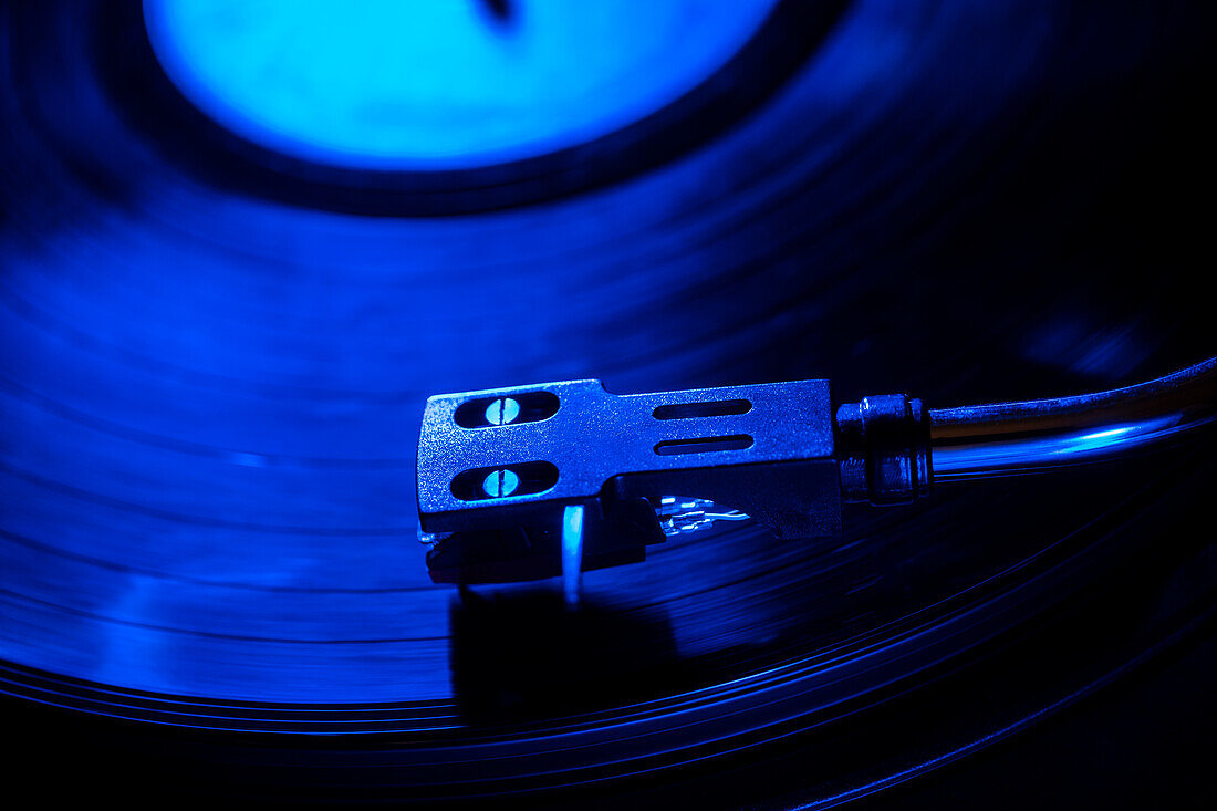 Nahaufnahme einer Plattenspielernadel auf einer Schallplatte in blauem Licht