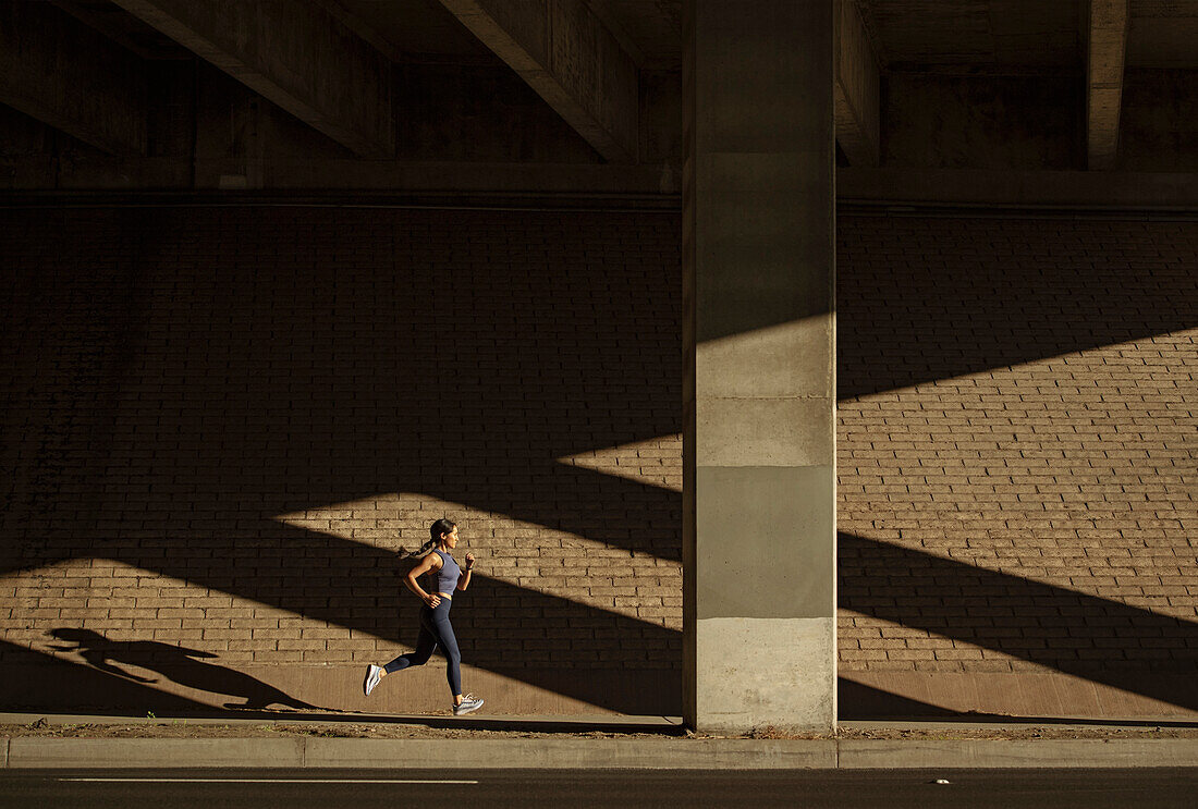 Frau joggt in der Nähe einer Backsteinmauer im Sonnenlicht
