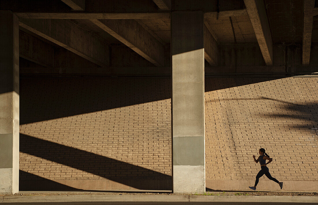 Frau joggt nahe einer Mauer im Sonnenlicht