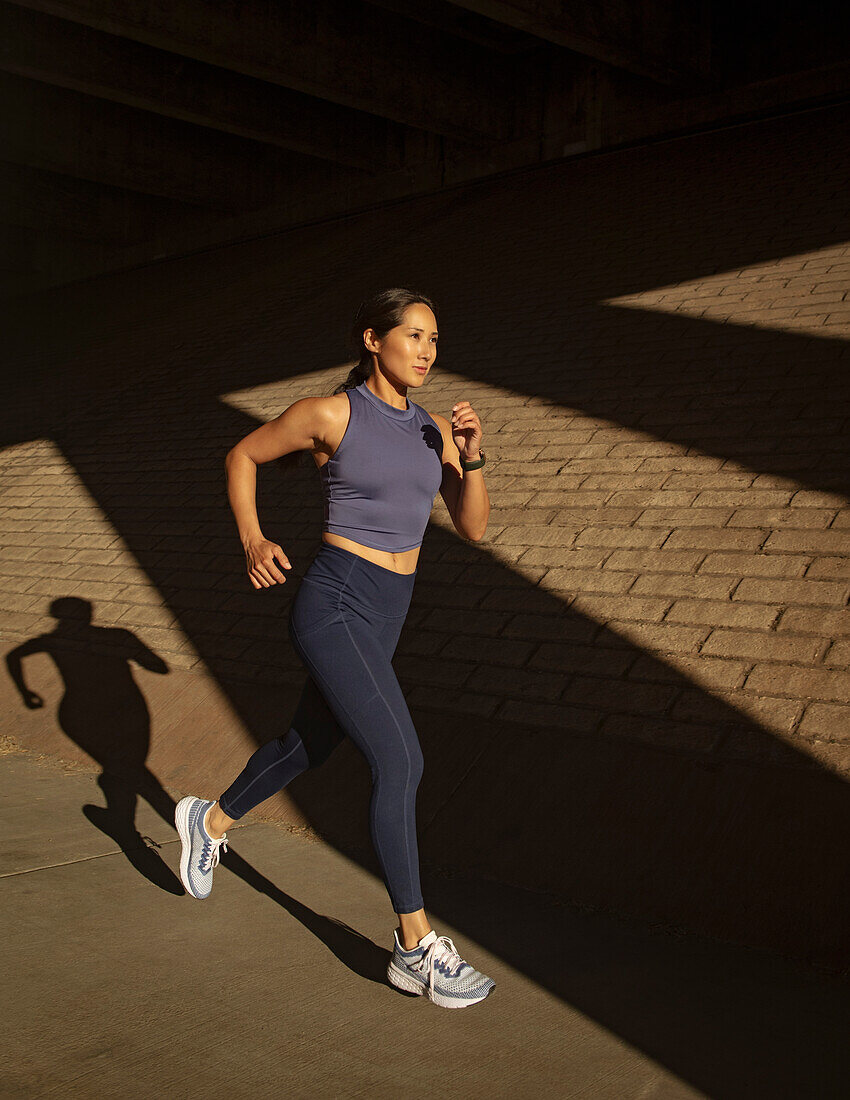 Frau joggt in der Nähe einer Backsteinmauer im Sonnenlicht