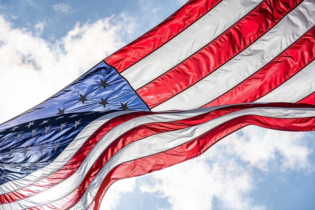 Low angle view of American flag waving in wind against sky