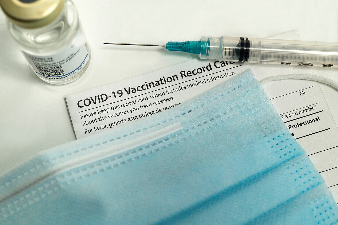 Syringe on Covid-19 vaccination record card, face mask and vial