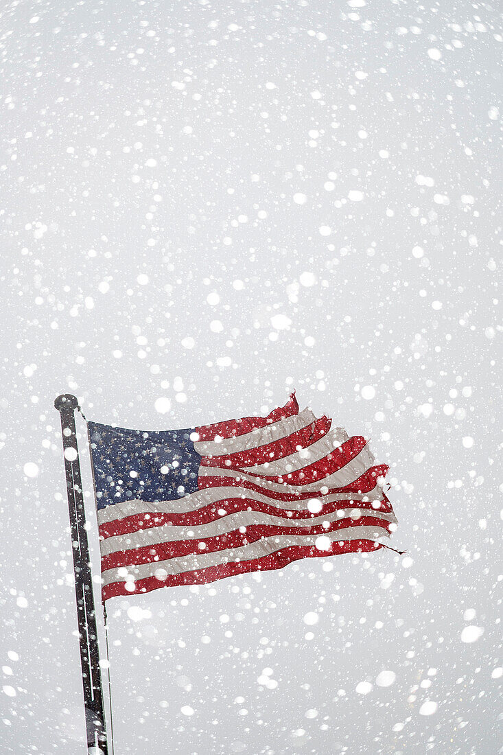 Torn American flag on flag pole with falling snow