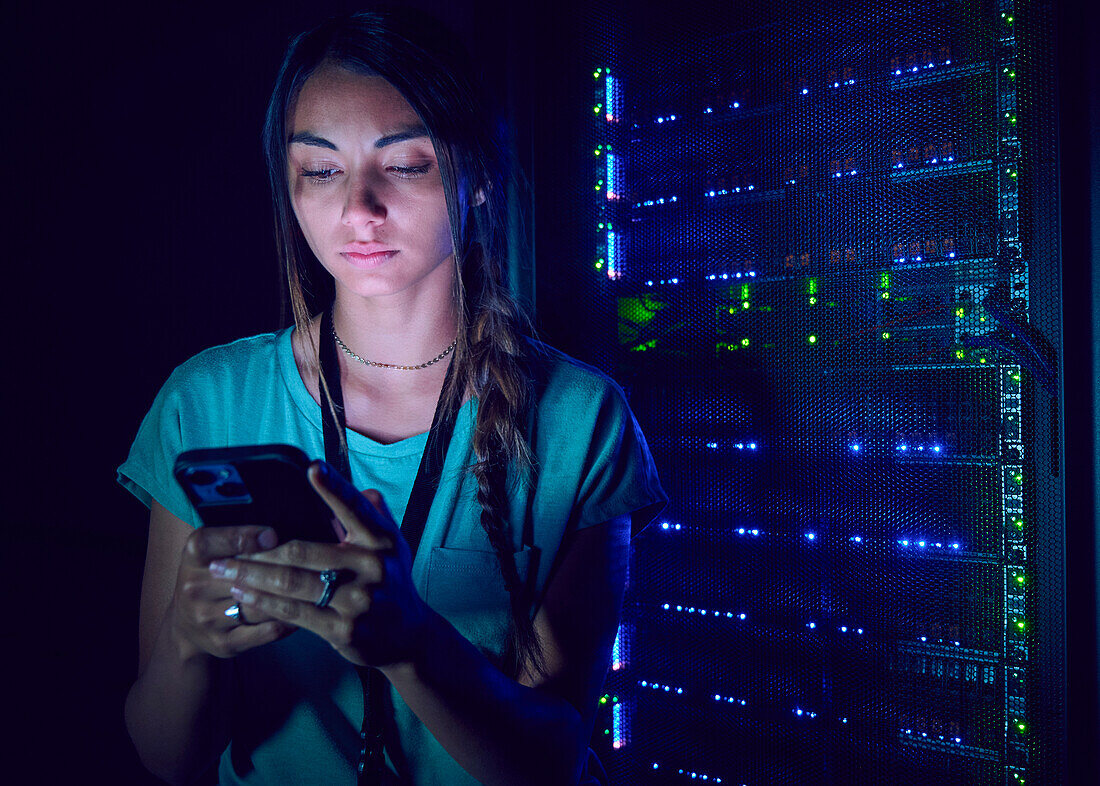 Female technician using smart phone in server room