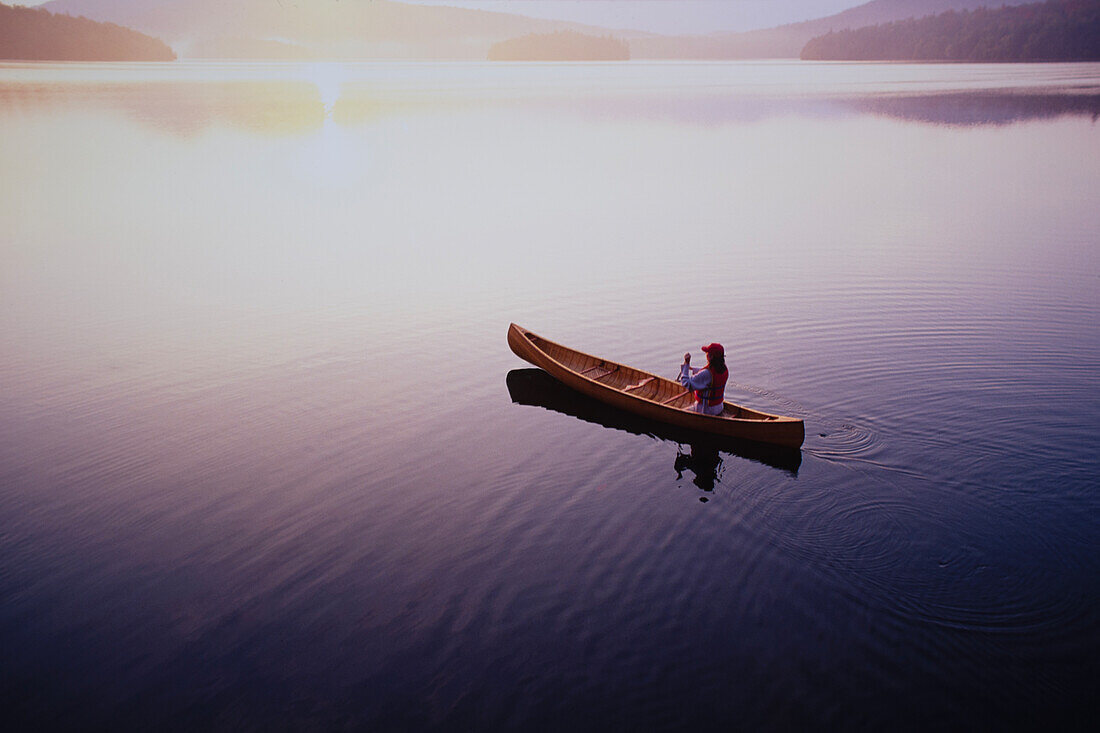 Blick von oben auf eine Frau, die bei Sonnenaufgang auf dem Lake Placid Kanu fährt, Adirondacks State Park