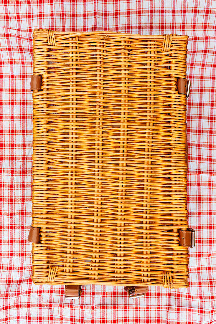 Overhead view of closed wicker picnic basket on plaid tablecloth