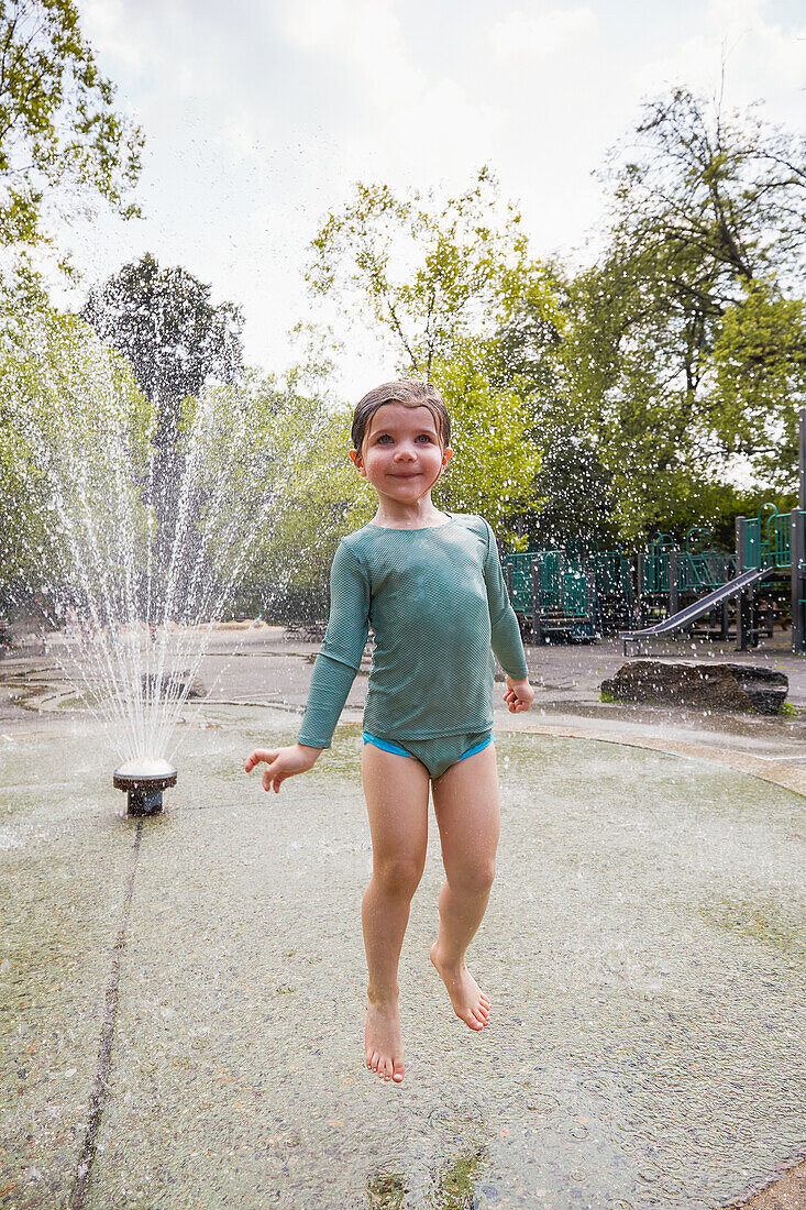 Girl (2-3) jumping in sprinklers