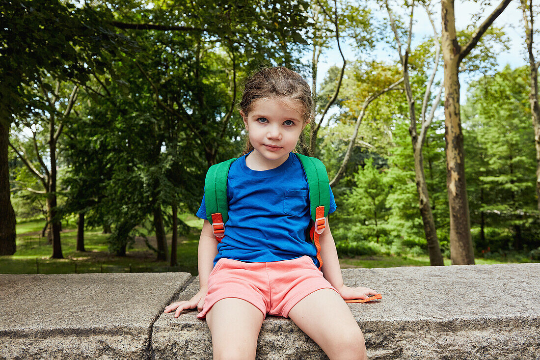 Portrait of girl (2-3) with backpack sitting on wall