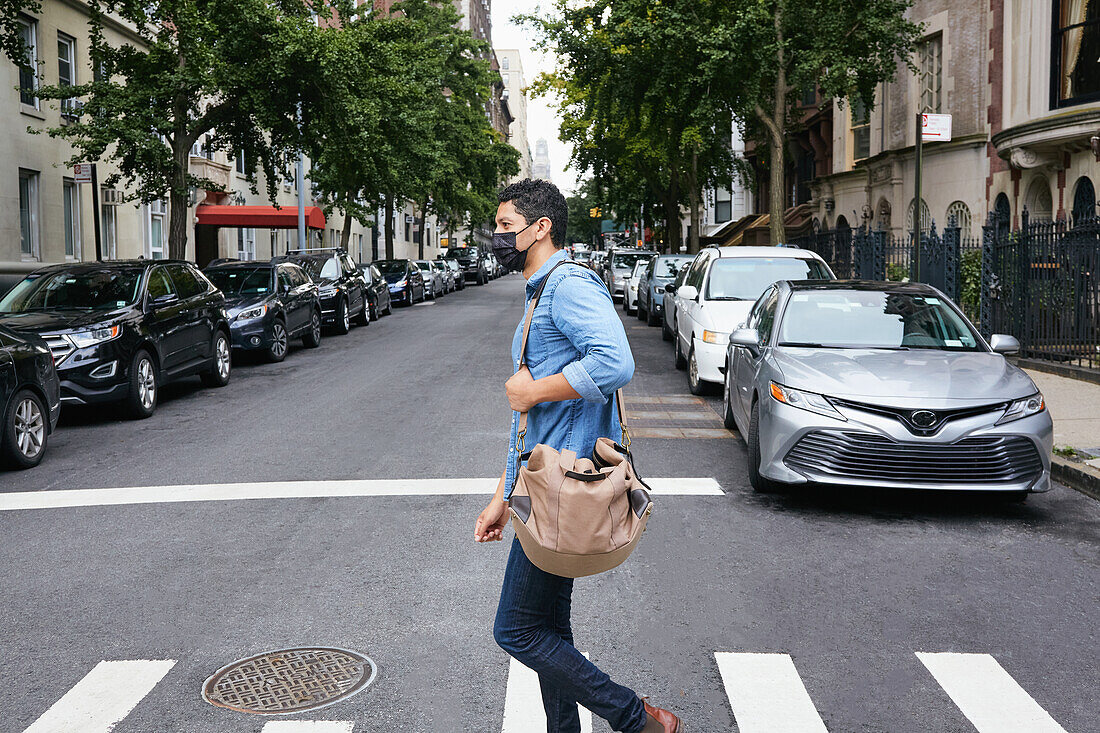 USA, New York, New York City, Mann mit Gesichtsmaske beim Überqueren der Straße in der Stadt