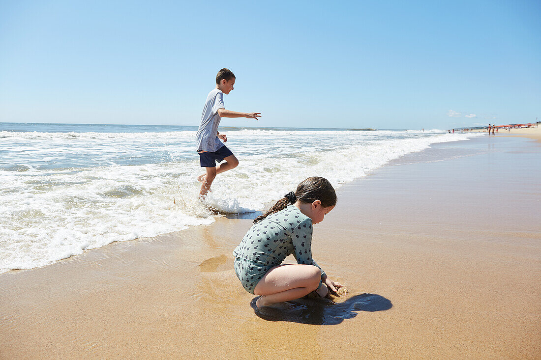 Boy (8-9) and girl (2-3) playing on beach 