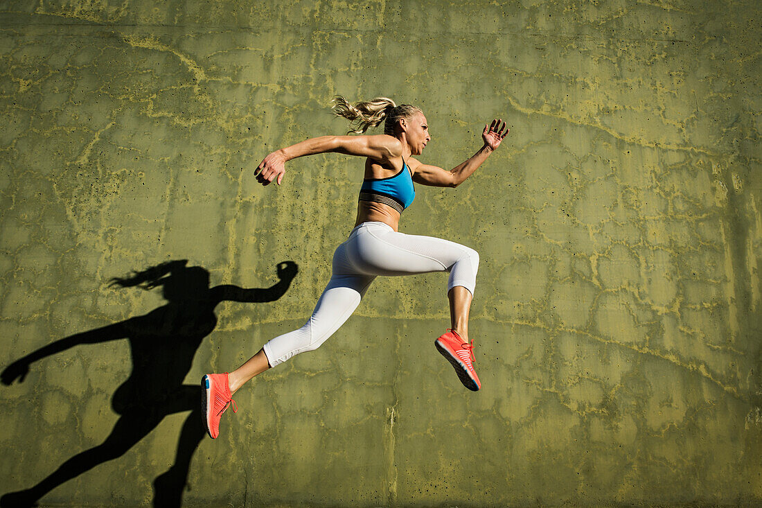 Athlete woman jumping against wall