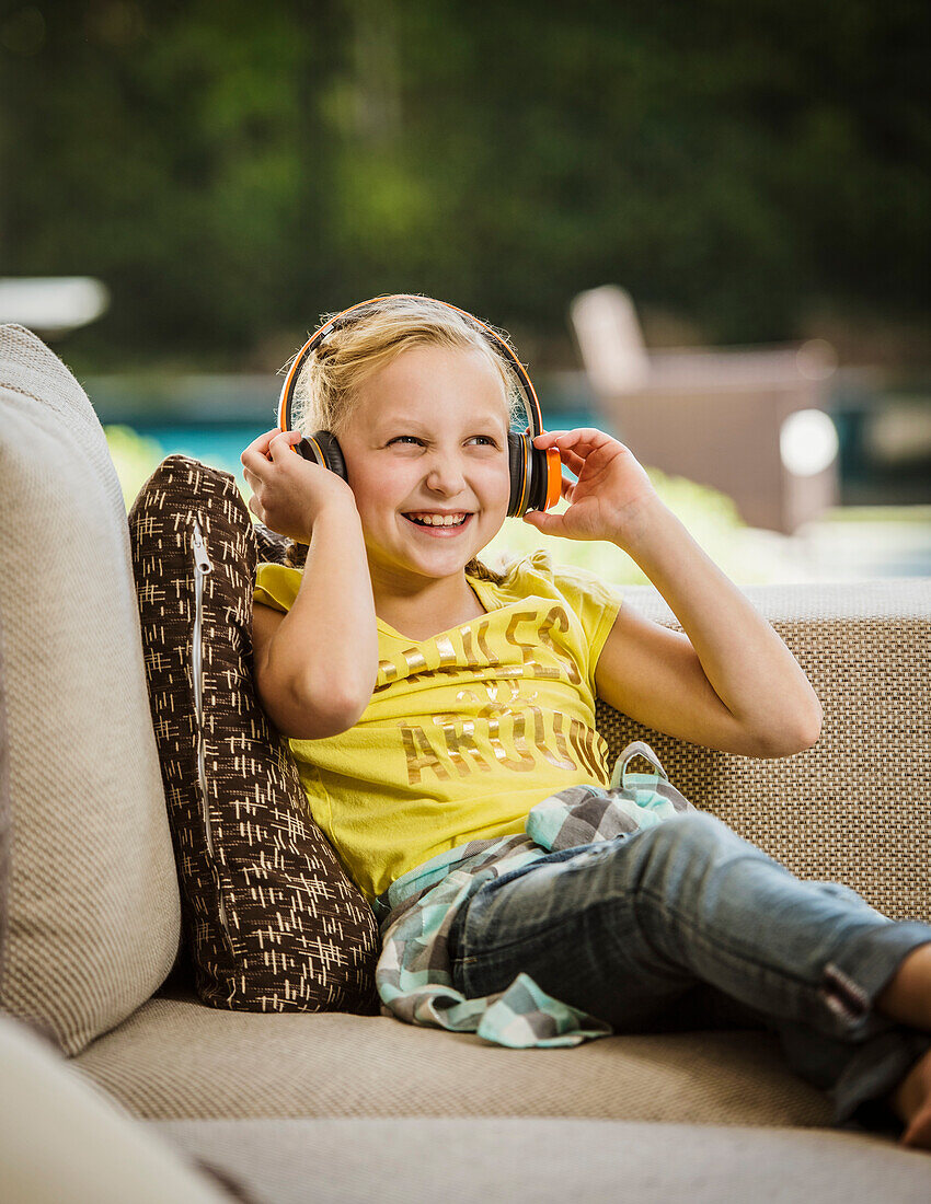 Smiling girl (10-11) with headphones sitting on sofa