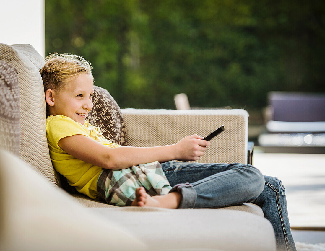 Smiling girl (10-11) with remote control sitting on sofa