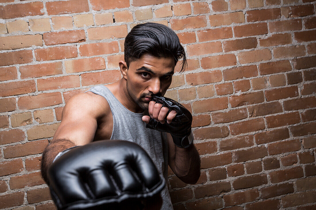 Porträt eines Mannes mit Boxhandschuhen an einer Backsteinmauer