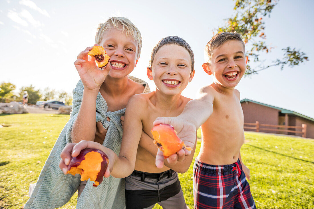 Porträt von Jungen (8-9) ohne Hemd, die Pfirsiche im Garten essen