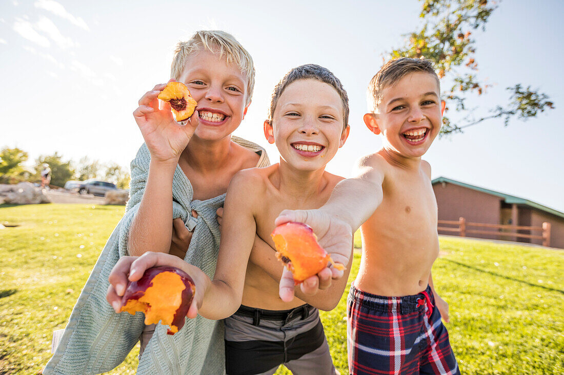 Portrait of shirtless boys (8-9) eating peaches in garden