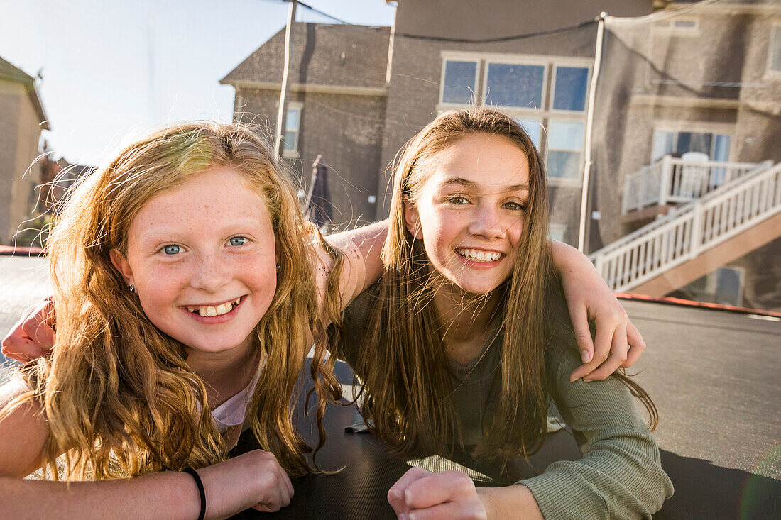 Portrait of smiling girls (10-11, 12-13) on trampoline in front of house
