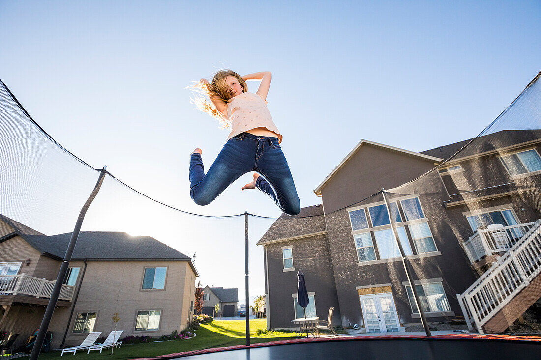 Mädchen (10-11) springt auf dem Trampolin vor dem Haus
