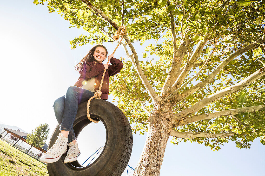 Smiling girl (12-13) on tire swing in garden