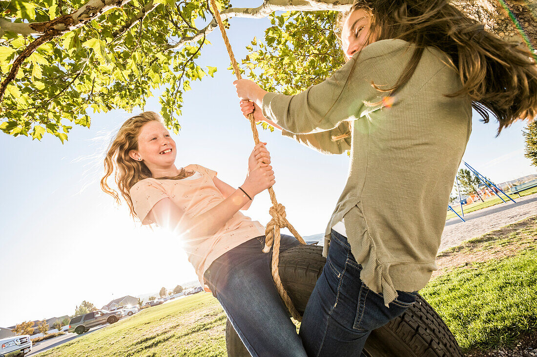 Lächelnde Mädchen (10-11, 12-13) auf der Reifenschaukel im Garten