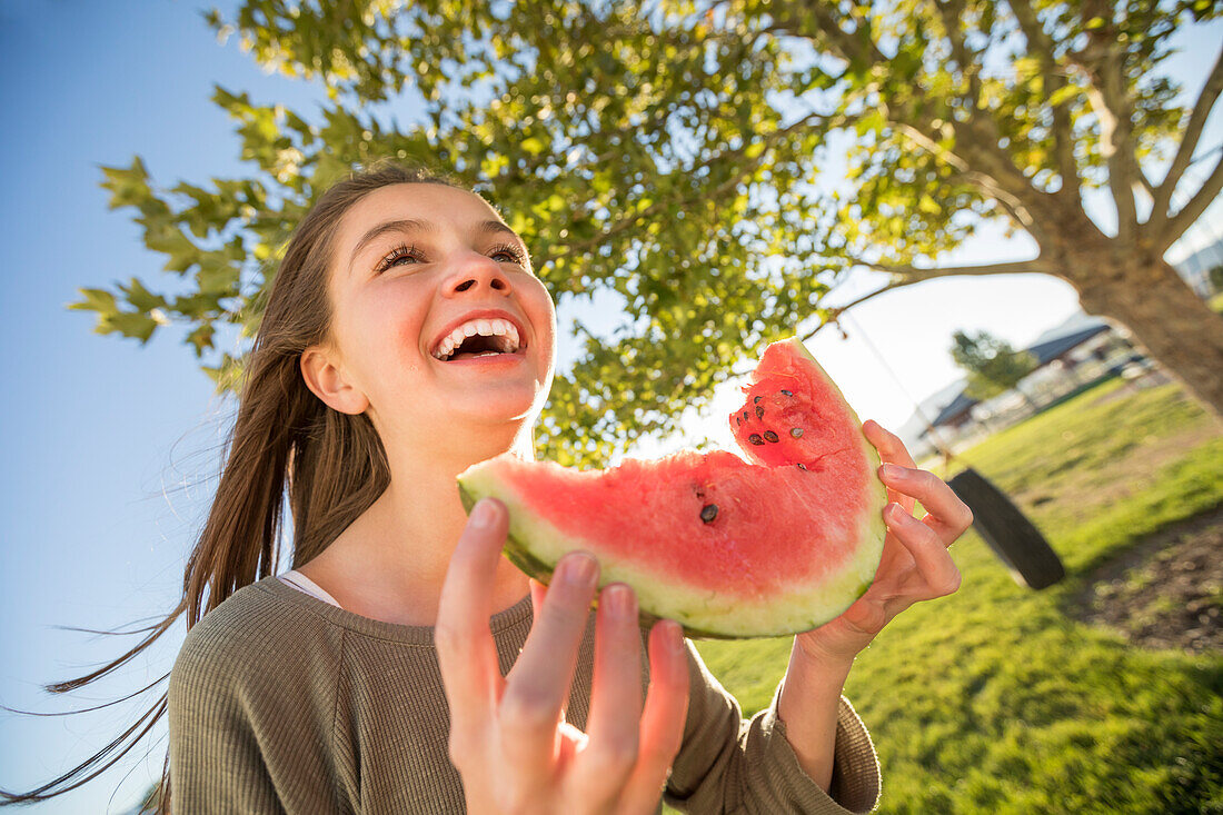 Lächelndes Mädchen (12-13) hält eine Scheibe Wassermelone im Garten