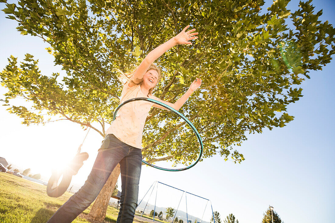 Mädchen (12-13) dreht Hula-Hoop-Reifen, Schwester (10-11) auf der Reifenschaukel im Hintergrund