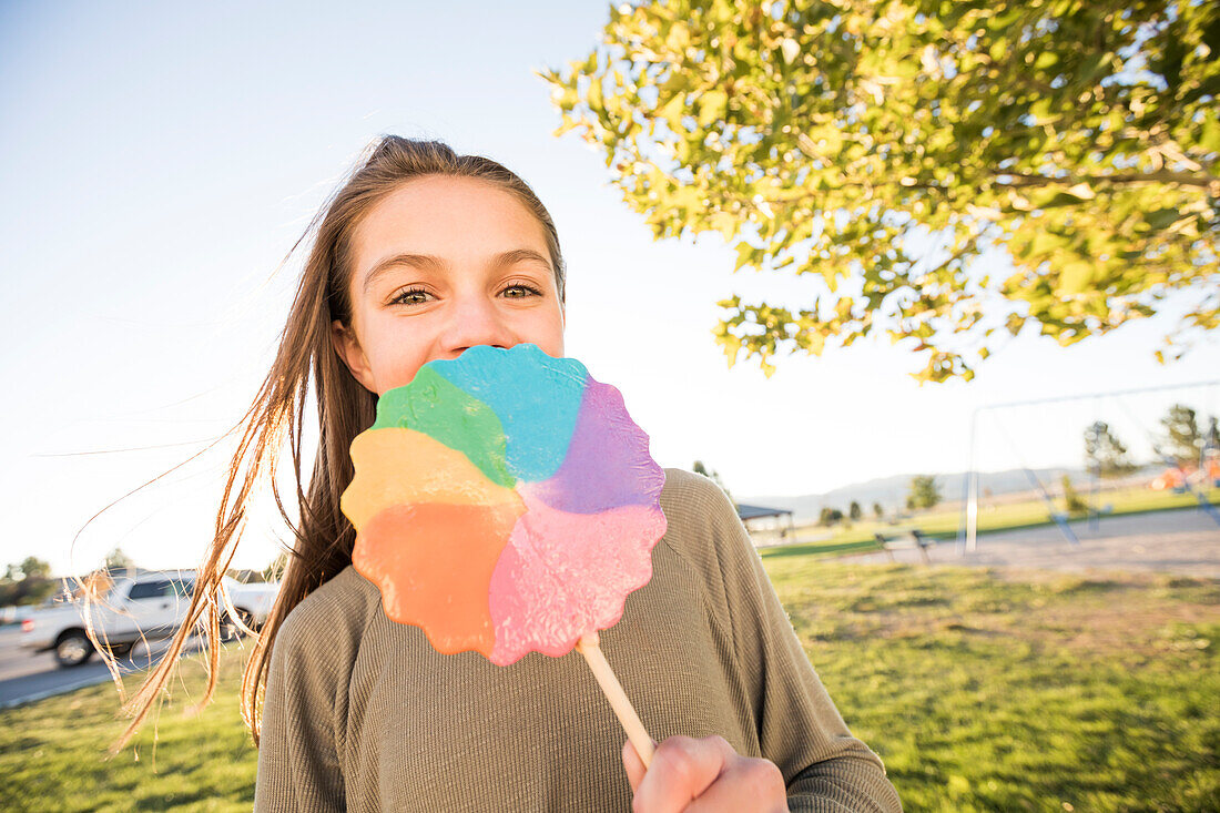 Portrait of girl (12-13) with colorful lollipop in park