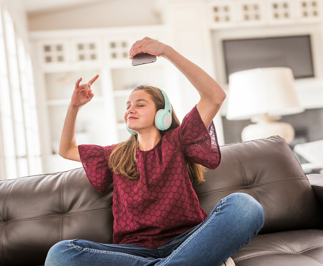 Smiling girl (12-13) with headphones and smart phone on sofa