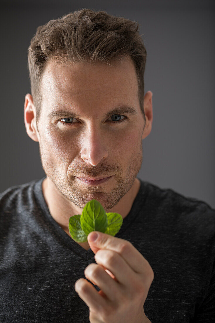 Studio portrait of man holding fresh mint leaves