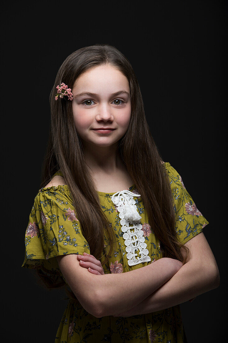 Studio-Porträt von lächelnden Mädchen (10-11) in grünem Kleid mit Blume im Haar