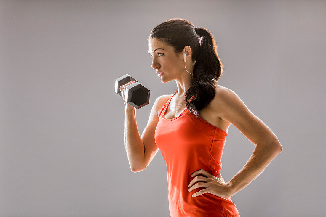 Studio shot of athletic woman in red sleeveless top exercising with dumbbell