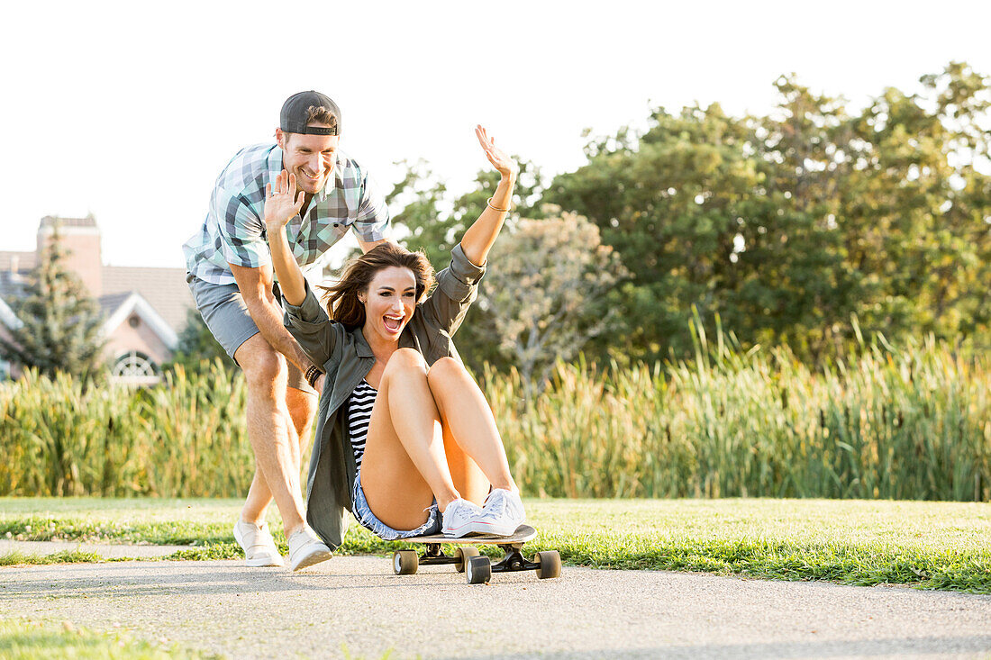 Mann schiebt Frau auf Longboard im Park 