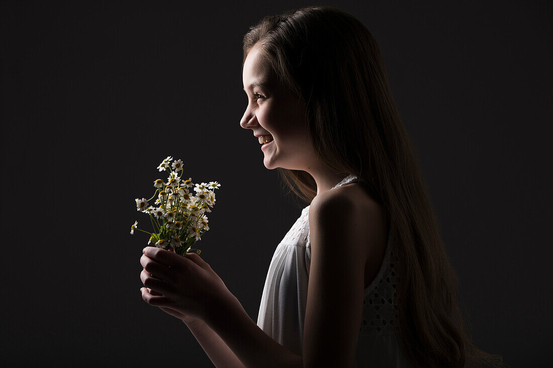 Profil eines lächelnden Mädchens (10-11) mit einem Strauß Wildblumen vor schwarzem Hintergrund