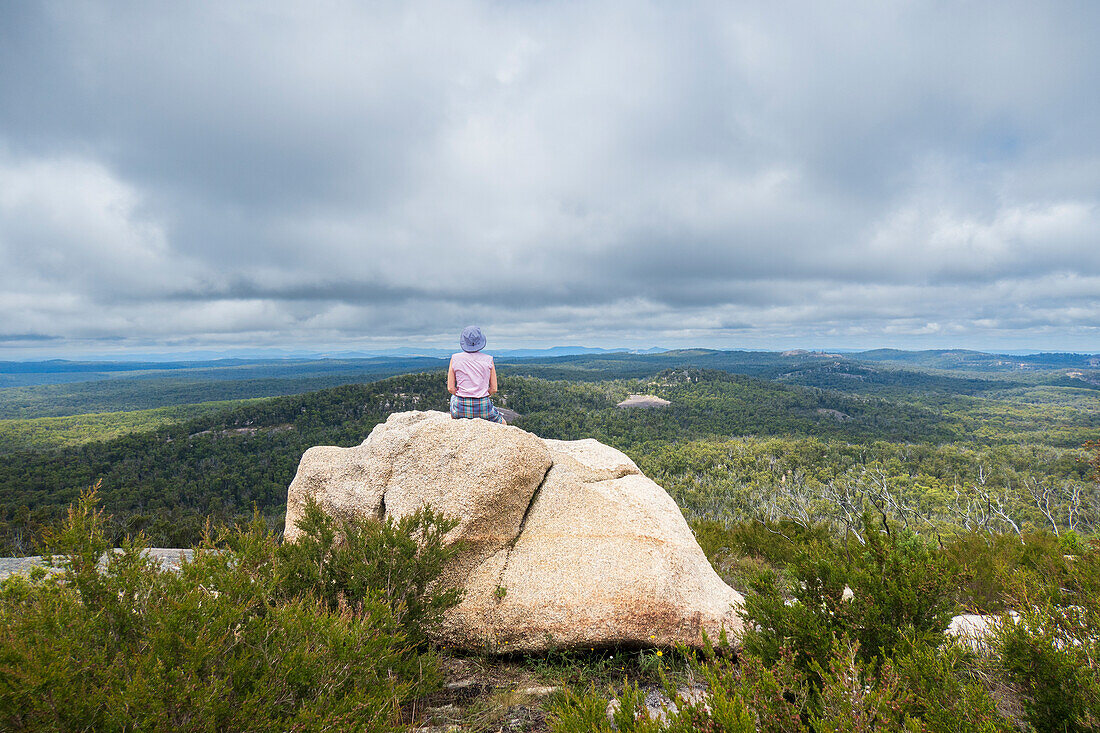 Australien, New South Wales, Bald Rock National Park, Frau sitzt auf einem Felsen und blickt umher