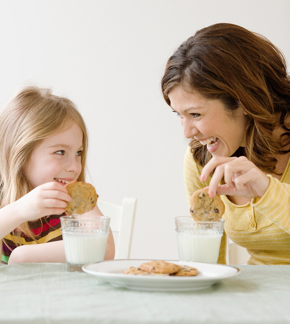 Mutter und Tochter tunken Kekse in Milch