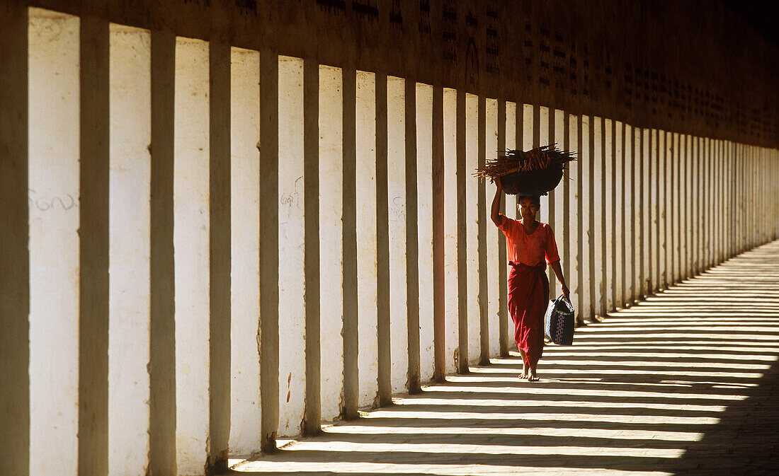 Myanmar, Bagan, Bezirk Mandalay, Frau, die in der Säulenhalle der Schwezigon-Pagode spazieren geht und Holz auf dem Kopf trägt