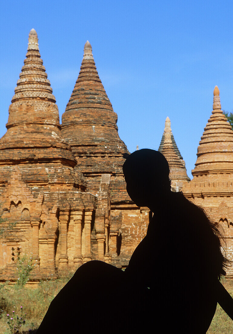 Myanmar, Bagan, Division Mandalay, Silhouette einer jungen Frau, die vor einer buddhistischen Pagode sitzt