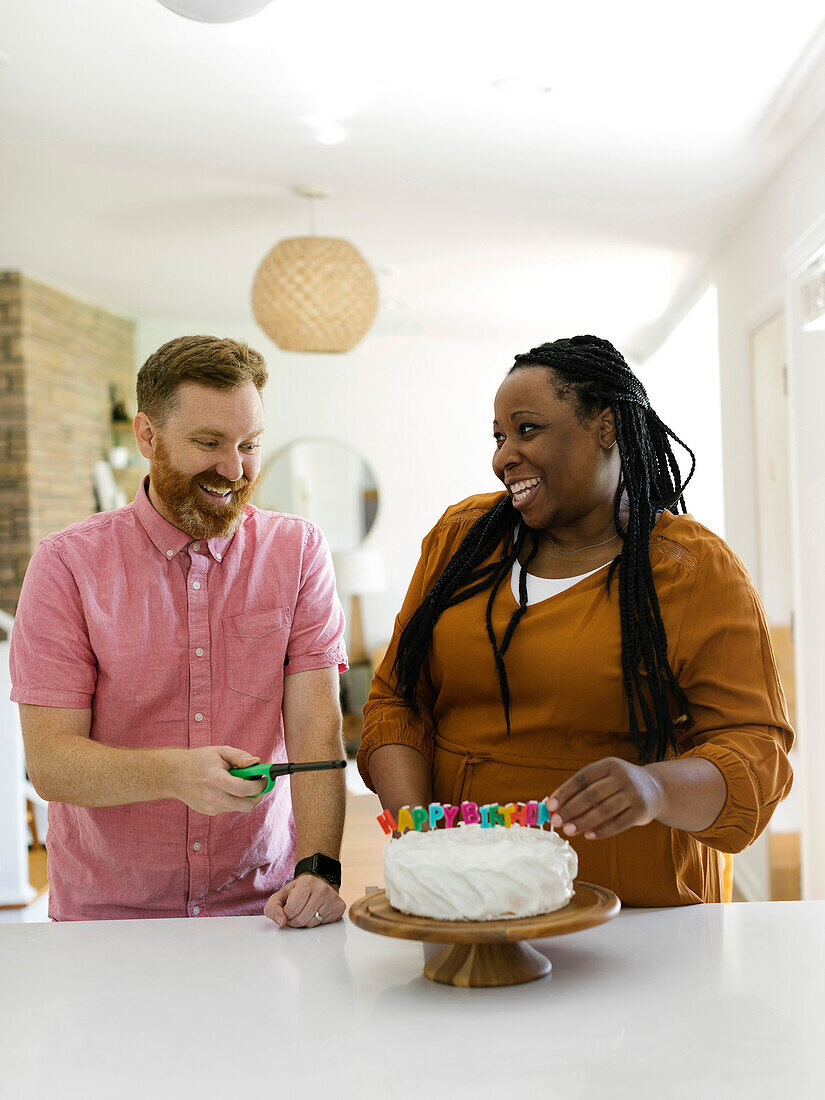 Smiling couple lighting birthday candles on cake